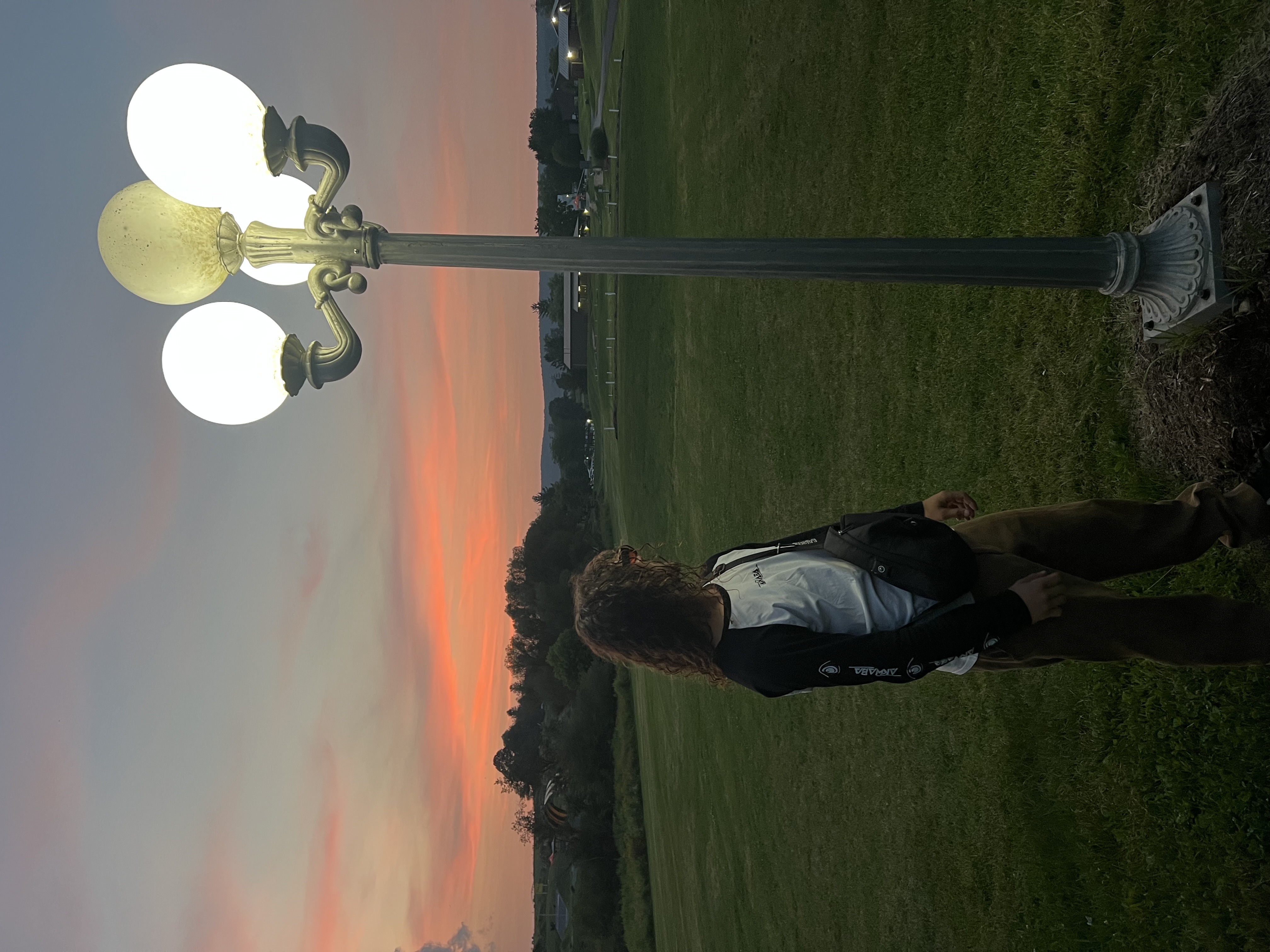 Matis staat bij zonsondergang buiten naast een verlichte lantaarnpaal
